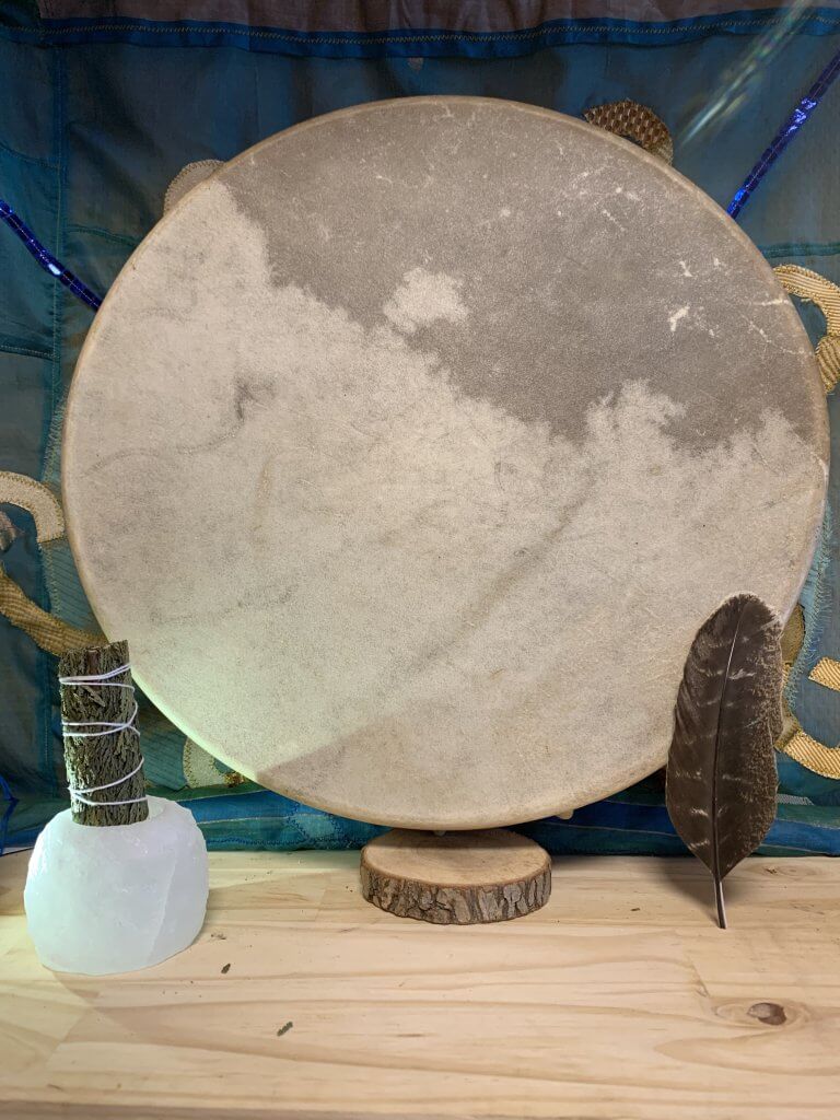 Image de la face avant d'un tambour chamanique, mettant en vedette une peau de bison tendue précisément sur le cadre rond. La peau, choisie pour sa robustesse et ses qualités acoustiques uniques, présente une texture riche et une couleur allant du brun foncé au doré, avec des variations naturelles et des marques qui témoignent de l'authenticité du matériau. Le centre du tambour, souvent considéré comme le cœur ou le point focal dans de nombreuses traditions chamaniques, peut être marqué ou laissé naturel, servant de guide pour le joueur. La surface de la peau est lisse, prête à résonner avec des sons profonds et enveloppants lorsqu'elle est frappée avec la mailloche, invitant à la méditation et à la connexion spirituelle. Les bords du tambour révèlent le soin apporté à l'attache de la peau au cadre, assurant une tension uniforme pour une qualité sonore optimale